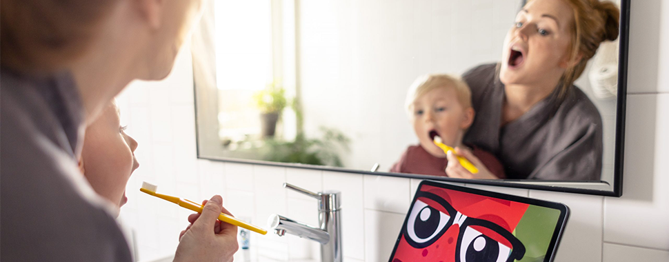 Vuxen borstar tänder på litet barn, som gapar enligt instruktionerna i Folktandvårdens app Rocka munnen. 